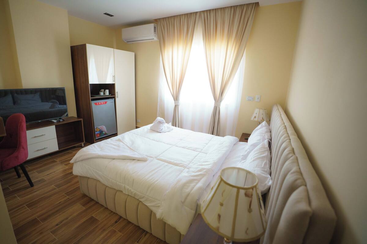 A hotel room with a bed, a desk with a chair, a wardrobe, and a window with curtains.
