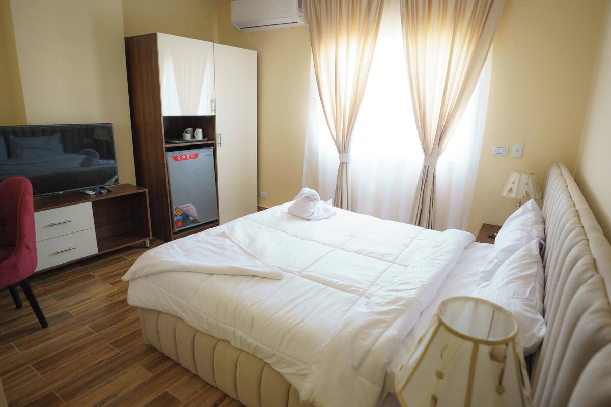 A hotel room with a bed, a wardrobe, a desk with a television, and a lamp.