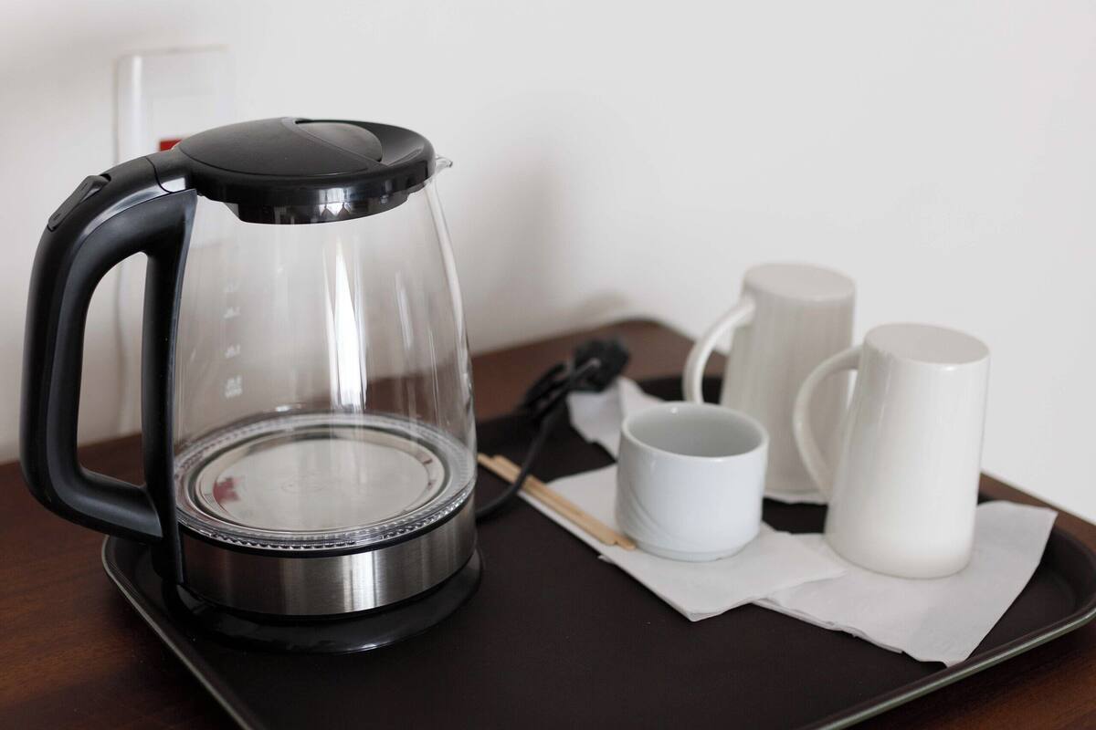 A coffee maker on a tray with two white mugs.