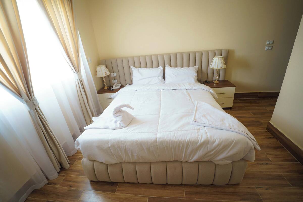 A neatly made bed with white linens and a decorative towel, a bedside lamp, and a nightstand with a phone.