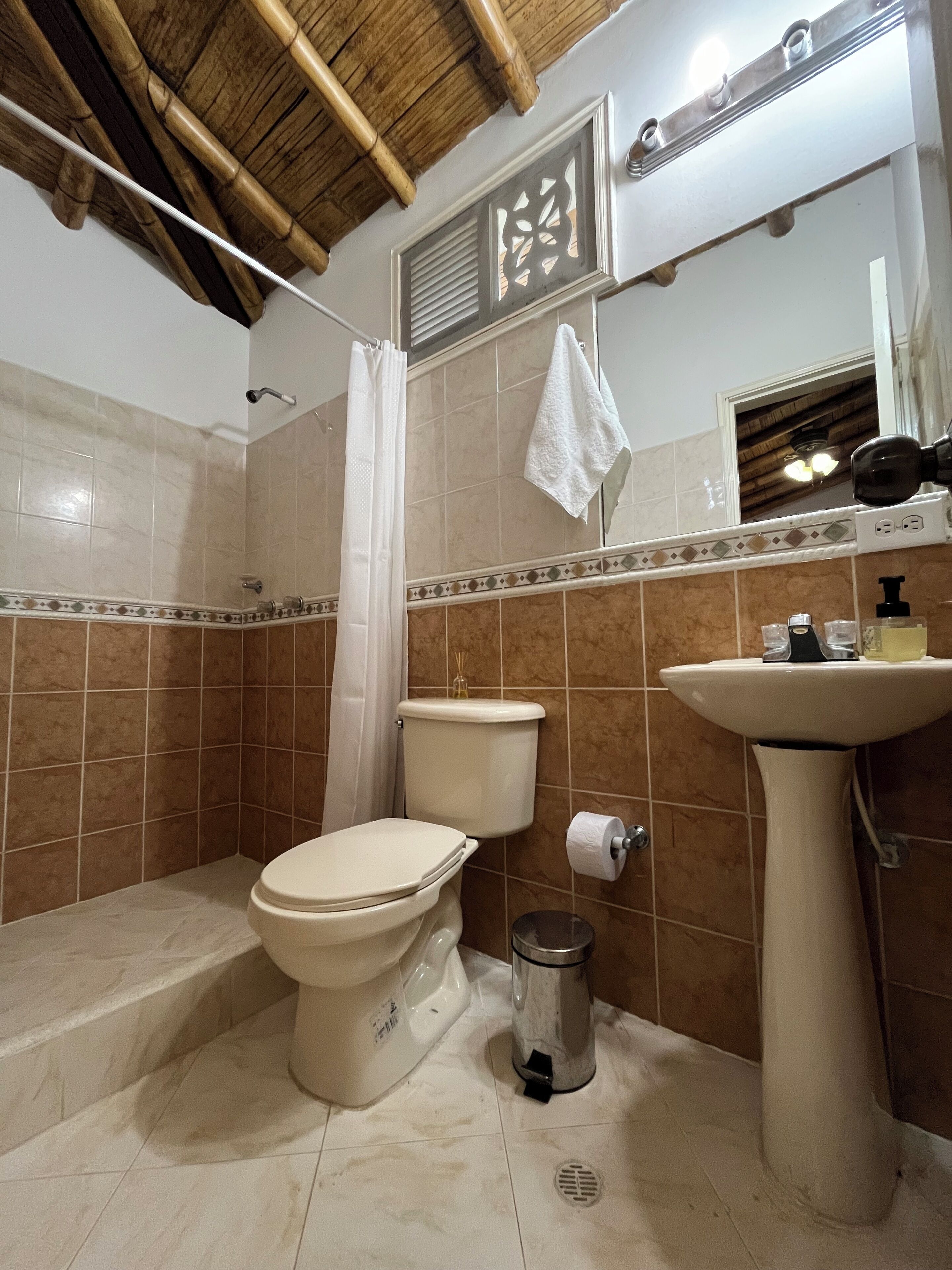 A bathroom with a toilet, sink, shower, and a towel hanging on the wall.