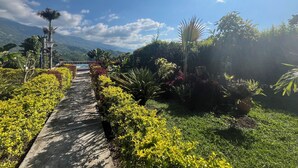 A pathway leading through a garden with various plants and a view of distant mountains. - Finca Hotel San Miguel (Calarcá)