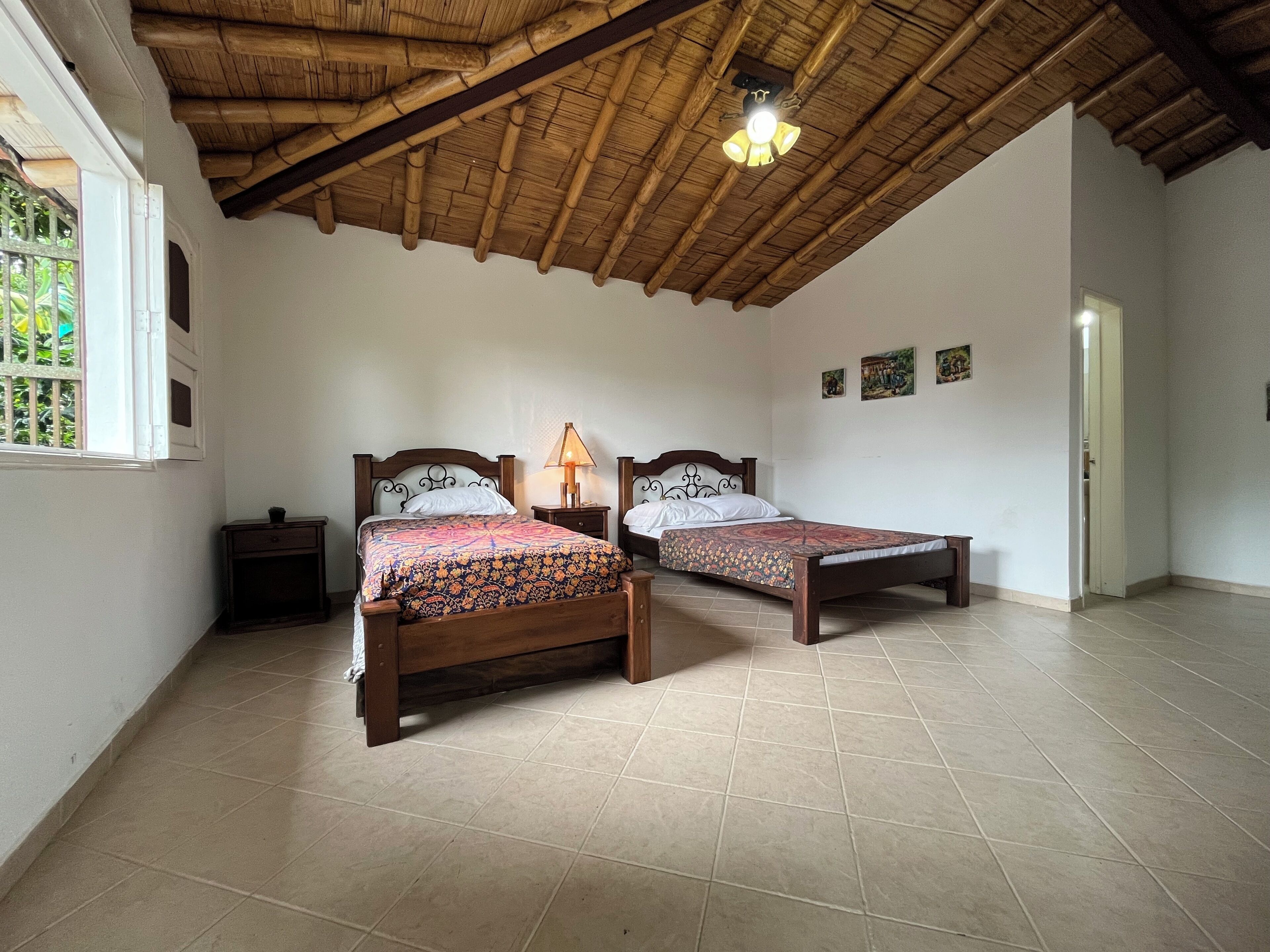 A room with two wooden beds, a ceiling fan, and a window with a view of greenery.
