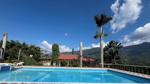 A swimming pool with a red and beige tiled deck, surrounded by palm trees and a mountain backdrop. - Finca Hotel San Miguel (Calarcá)