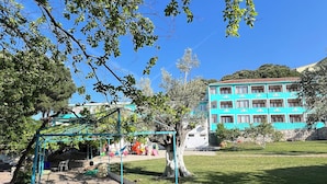 A playground with swings and slides, a grassy area, and a building with blue and white exterior in the background.