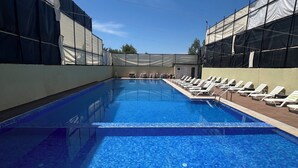 A swimming pool with clear blue water, surrounded by sun loungers and a covered area with a view of the sky.