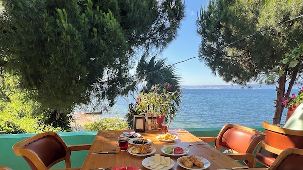 A wooden table set with plates of food, including watermelon, olives, and cheese, overlooking a body of water.