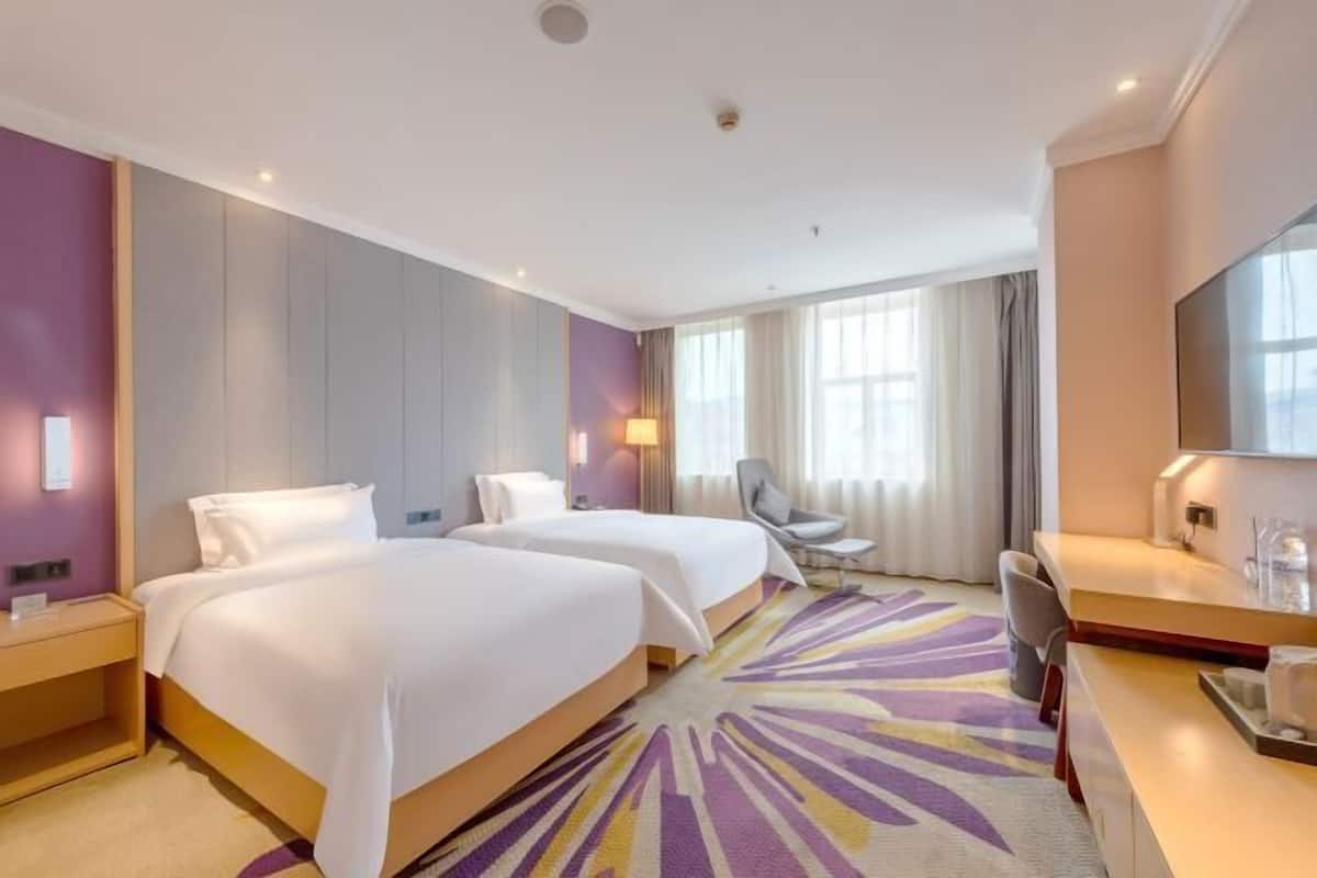 A hotel room with two beds, a desk, a chair, a TV, and a large window.
