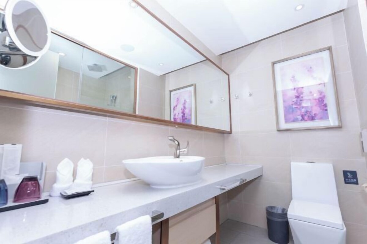 A modern bathroom with a large mirror, a white sink, and a toilet.