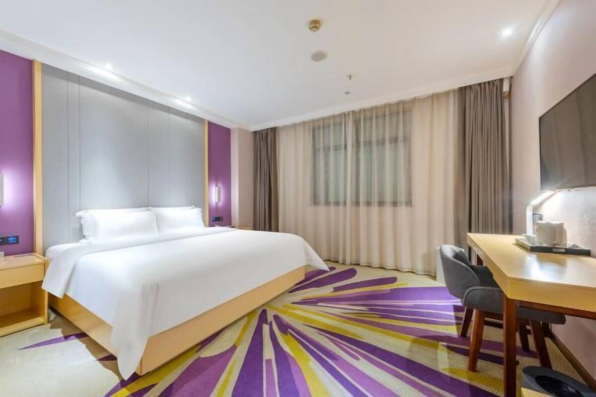 A hotel room with a bed, a desk, a chair, a TV, and a window with curtains.