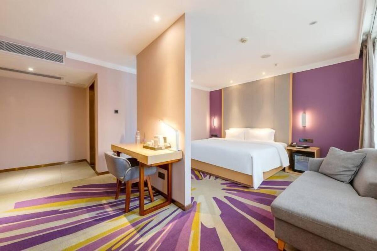 A hotel room with a bed, a desk, a chair, a sofa, and a colorful carpet.