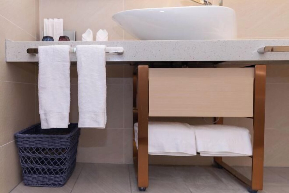 A bathroom with a large white sink, a towel rack with two towels, a wicker basket, and a wooden shelf.