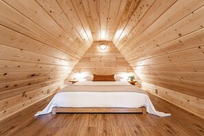 Un dormitorio acogedor con paneles de madera, una cama grande, dos mesitas de noche y un tragaluz circular.