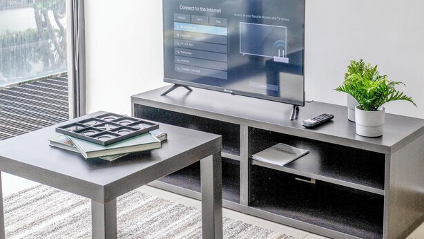 Una sala de estar moderna con un televisor de pantalla plana, una mesa de centro, una planta en maceta y un ventanal con vista a zonas verdes.