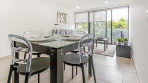 Un comedor moderno con una mesa de vidrio, cuatro sillas y vistas a un balcón con plantas en macetas.