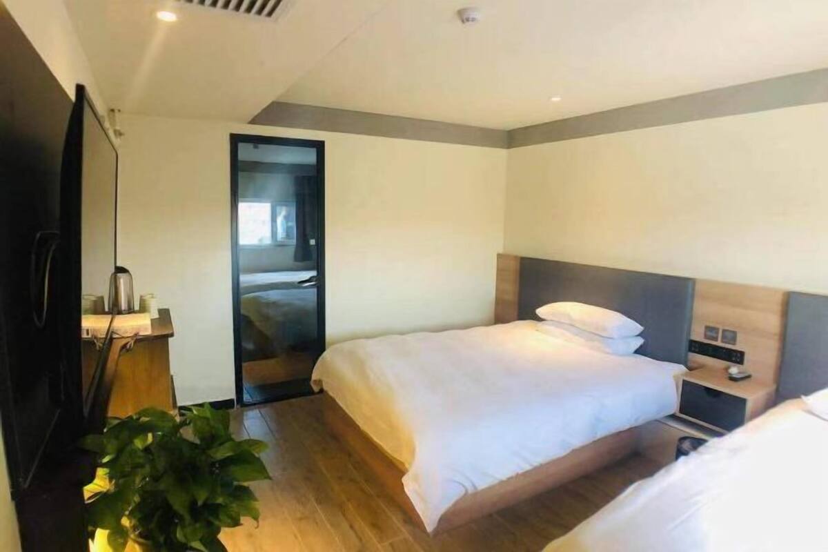 A hotel room with two beds, a wooden floor, a TV, a plant, and a door leading to a bathroom.