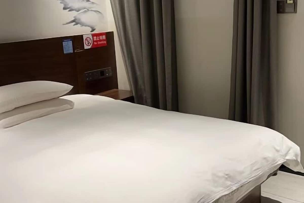 A hotel room with a bed, a headboard with a sign, curtains, and a wall with a painting.