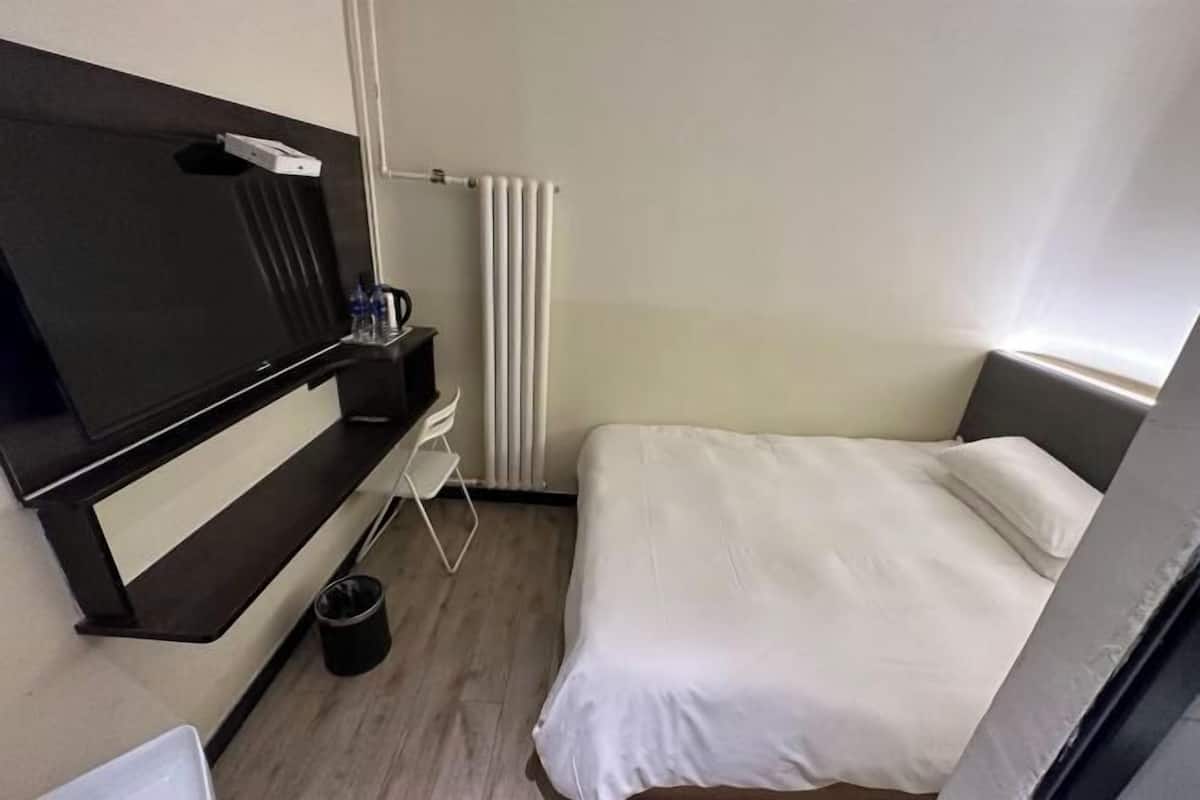 A hotel room with a bed, a TV mounted on the wall, a small table with a chair, and a radiator.