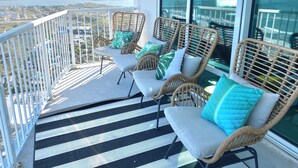 Een balkon met rieten stoelen en een zwart-wit gestreepte mat, met uitzicht op de kust.
