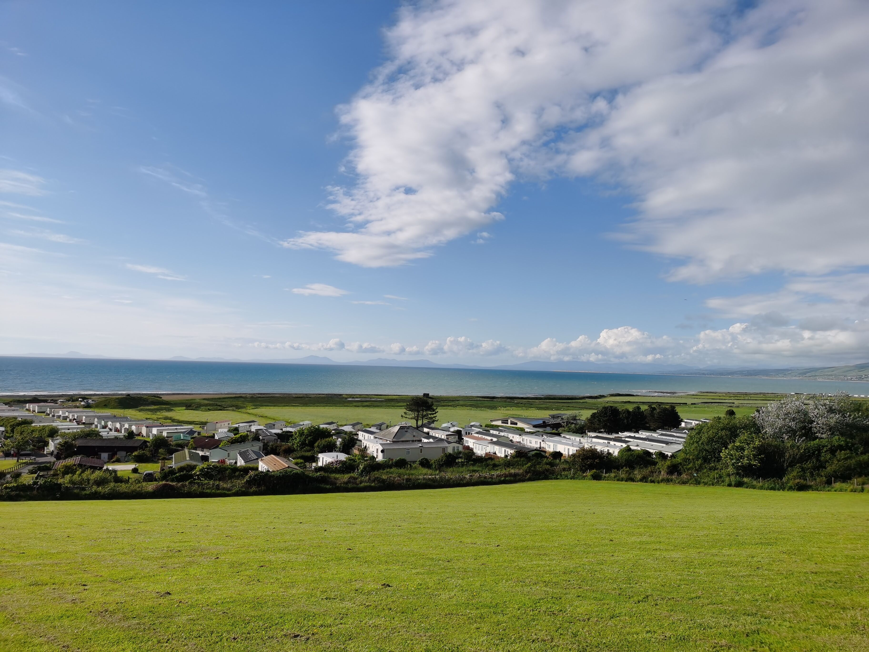 A coastal residential area with houses and a grassy field in the foreground.