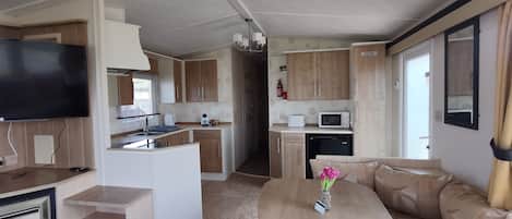 Een compacte camperkeuken met een eethoek, een flatscreen-tv en een kleine koelkast.