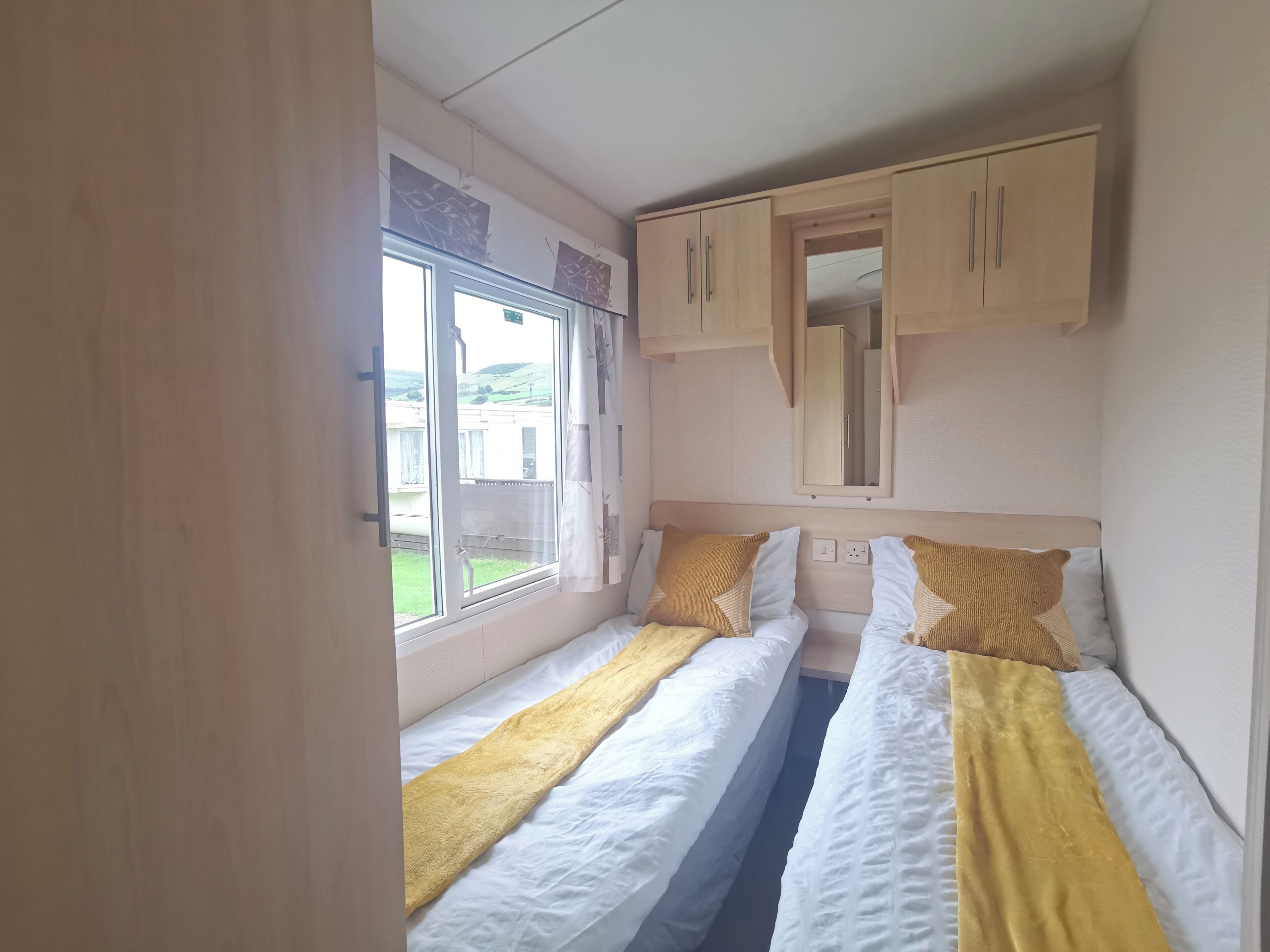 A compact bedroom with two beds, a window, and a wardrobe.