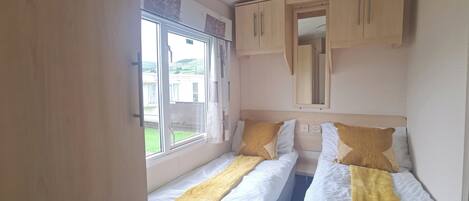 A compact bedroom with two beds, a window, and a wardrobe.
