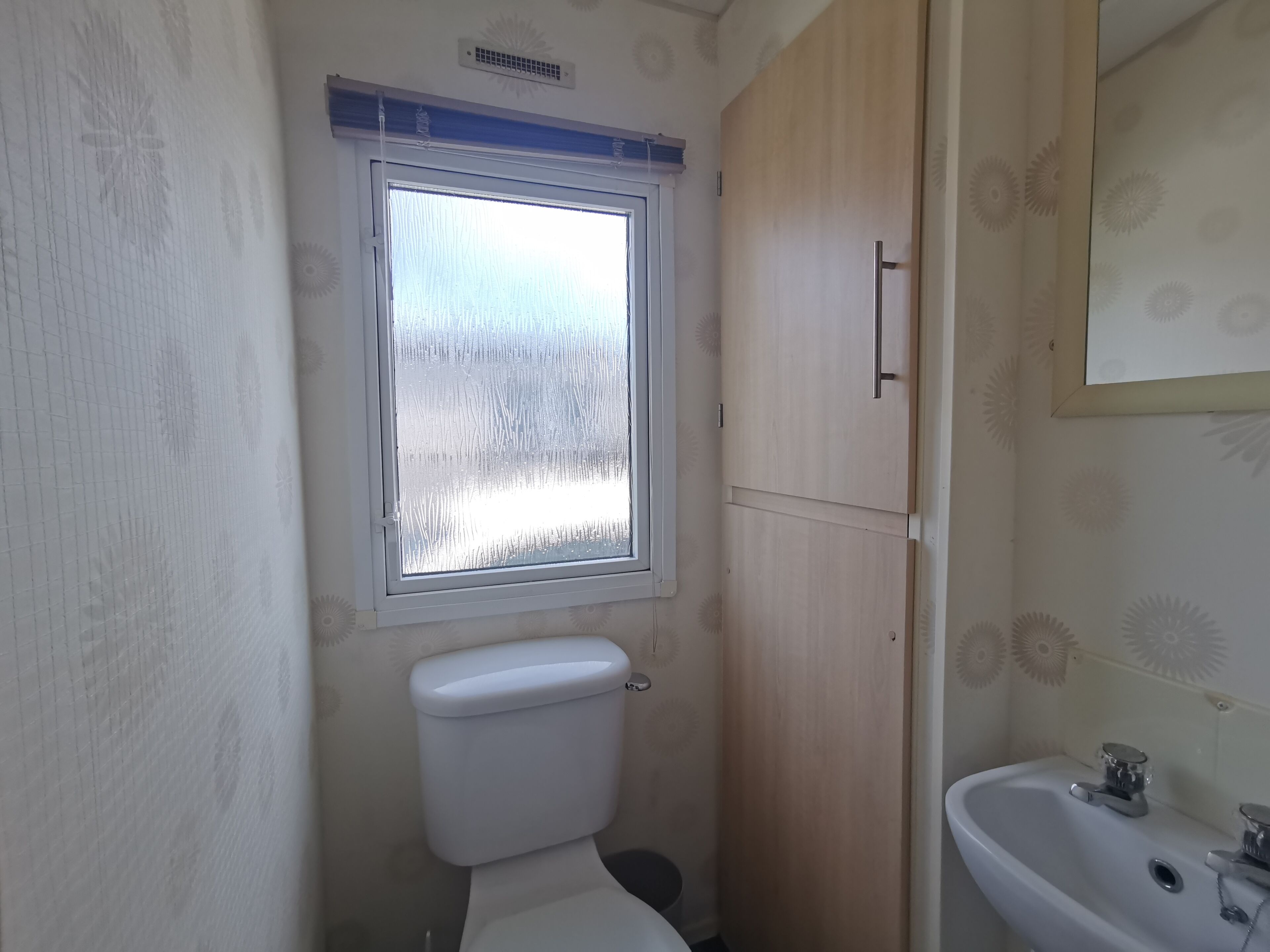 Ein kleines Badezimmer mit Toilette, Fenster und Waschbecken.
