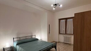 Quarto com cama, mesa de cabeceira, ventilador de teto, radiador e guarda-roupa.