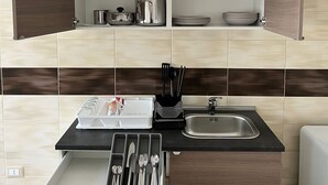 Cozinha compacta com armários abertos, pia e bancada com utensílios.