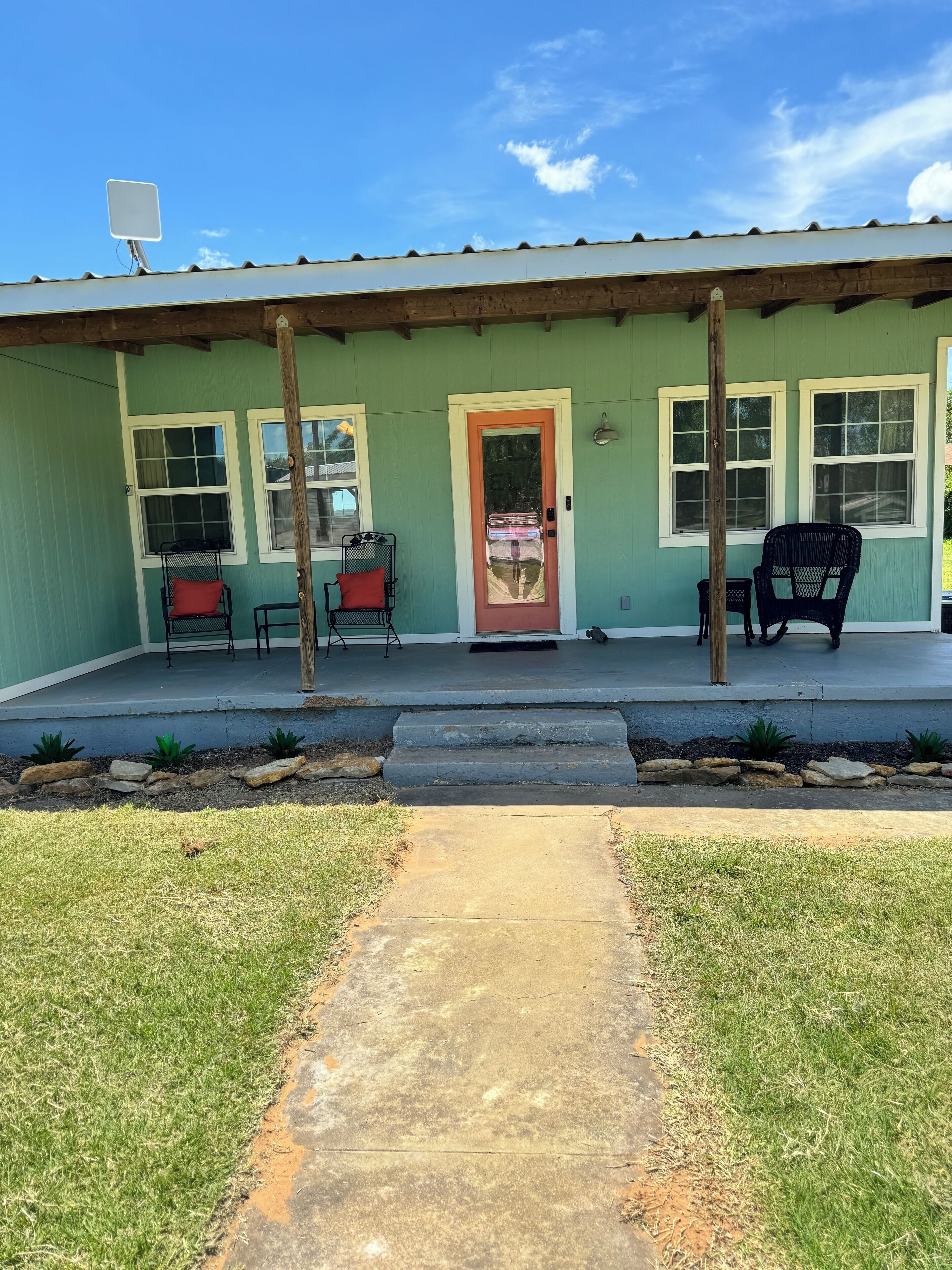 A building with a green exterior, a red door, and a porch with two chairs.