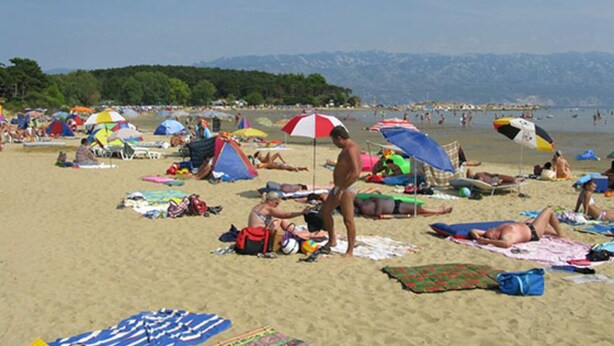 En overfyldt strand med folk, der solbader og svømmer, parasoller og strandtelt.