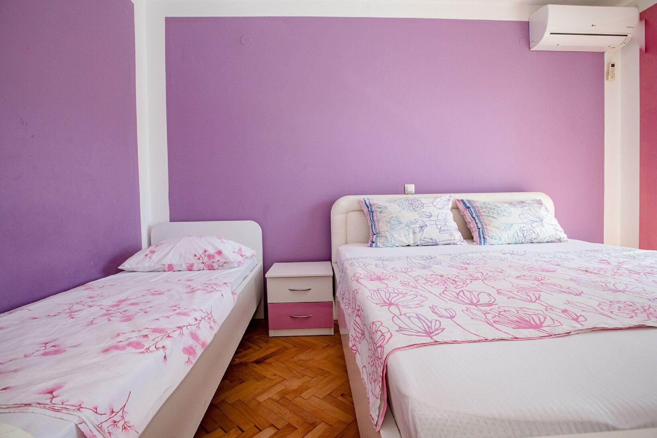 A bedroom with two single beds, a nightstand, and an air conditioning unit.