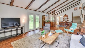 Een ruime woonkamer met een grote flatscreen televisie, houten vloeren, een eethoek met een houten tafel en stoelen, en een trap naar een ander niveau.