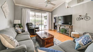 Ein Wohnzimmer mit grauem Sofa, einem Holztisch, einem Fernseher und einem Deckenventilator.