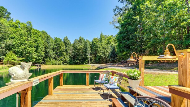A wooden deck with a bench and chairs, a fish sculpture, and a sign that reads "SWIM AT YOUR OWN RISK." - North Georgia Fall Escape for Hunting & Fishing (Ranger)