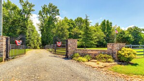 A gravel driveway leading to a gated entrance with a stone wall and a flag. - North Georgia Fall Escape for Hunting & Fishing (Ranger)