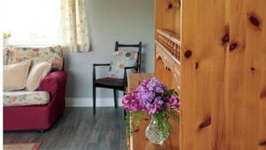 A living room with a red sofa, a wooden chair, a vase with purple flowers, and a wooden shelf with plates. - Farmer's Cottage (Nenagh)