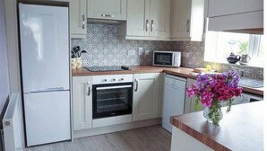 A kitchen with white cabinets, a microwave, a refrigerator, and a wooden countertop. - Farmer's Cottage (Nenagh)