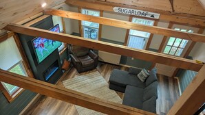 Un espacio habitable tipo loft con techo de madera, televisor, chimenea, sofá y mesa de comedor.
