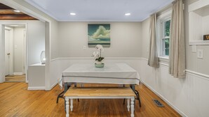 A dining area with a table set for two, a bench, a painting on the wall, and a window with curtains. - Lakeside, 2-Bedroom Cottage with Fire Pit in Dickson (Dickson)