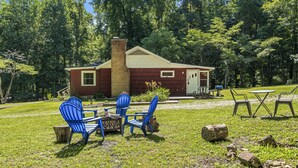 A lodge with a red exterior, a chimney, and a small porch. There are blue chairs and a table set up on the lawn. - Lakeside, 2-Bedroom Cottage with Fire Pit in Dickson (Dickson)