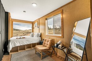 A bedroom with a bed, a chair, a painting, and a window with a view of a landscape. - The Nook Colorado - Park County (Jefferson)