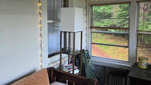 A cozy room with a plaid sofa, a small table, and a chair. There are string lights along the ceiling and a window with a view of greenery outside. - Cozy 2-bdrm, 3-season Adirondack cabin at tranquil Great Sacandaga Lake w/WiFi (Hadley)
