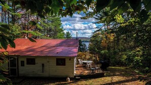 A rustic cabin with a red roof, surrounded by trees and a clear sky. - Cozy 2-bdrm, 3-season Adirondack cabin at tranquil Great Sacandaga Lake w/WiFi (Hadley)