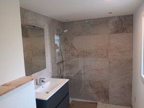 Une salle de bain moderne avec un mur de douche en marbre, un grand miroir et un lavabo intégré.