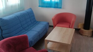 A room with a blue sofa, a red armchair, and a wooden coffee table. - Apartment 34m2 large terrace sea view 2km beaches gr34. Pink granite hillsides (Trelevern)