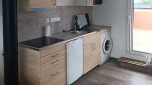 A compact kitchen with wooden cabinets, a microwave, a washing machine, and a sink. - Apartment 34m2 large terrace sea view 2km beaches gr34. Pink granite hillsides (Trelevern)