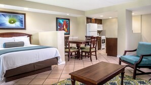 A hotel room with a bed, a dining table with chairs, a kitchenette, and a small armchair.