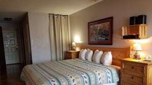 A neatly arranged hotel room with a bed, bedside tables, a lamp, a painting on the wall, and a door.